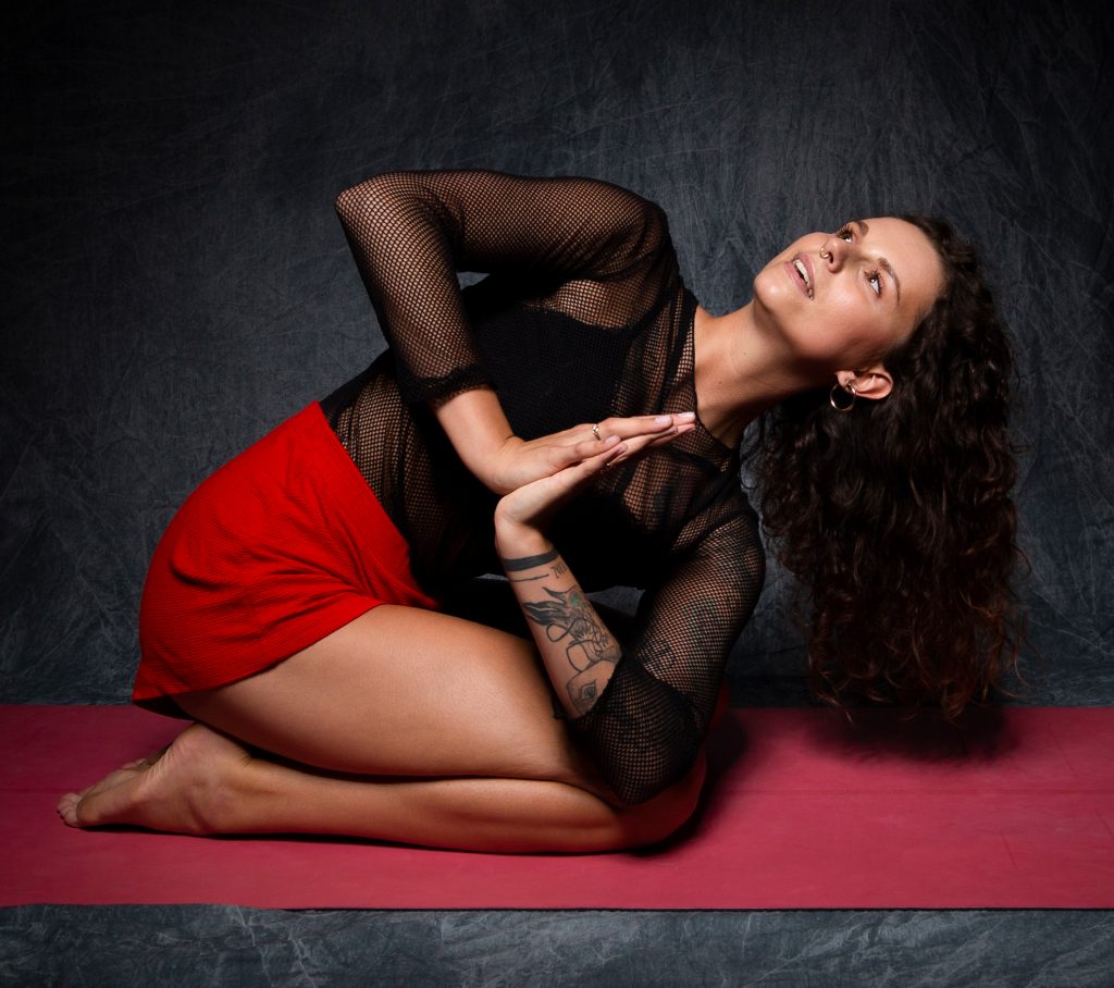 Kobieta siedzi na czerwonej macie, ćwiczy jogę
